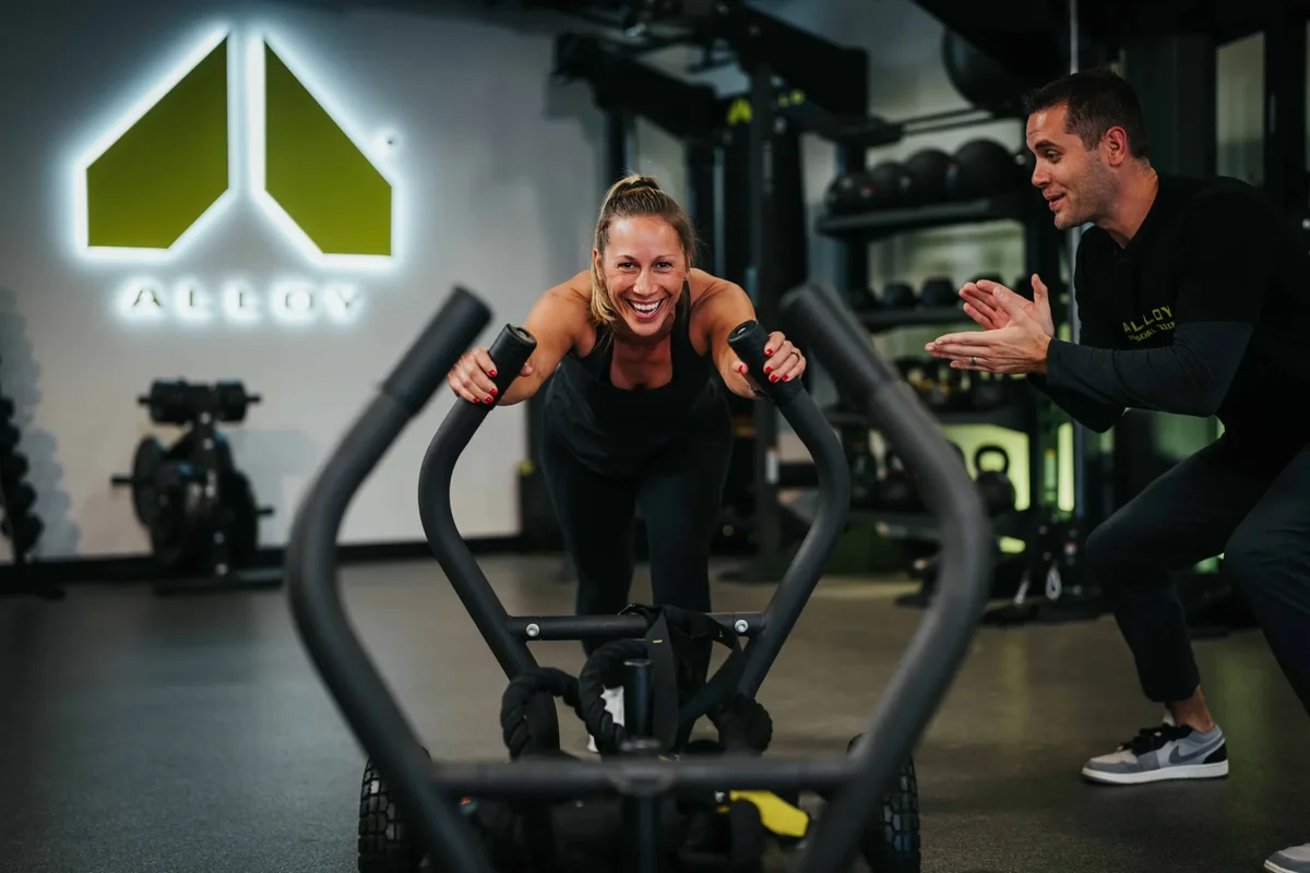 A coach cheers on a member pushing a weighted sled during a small group session