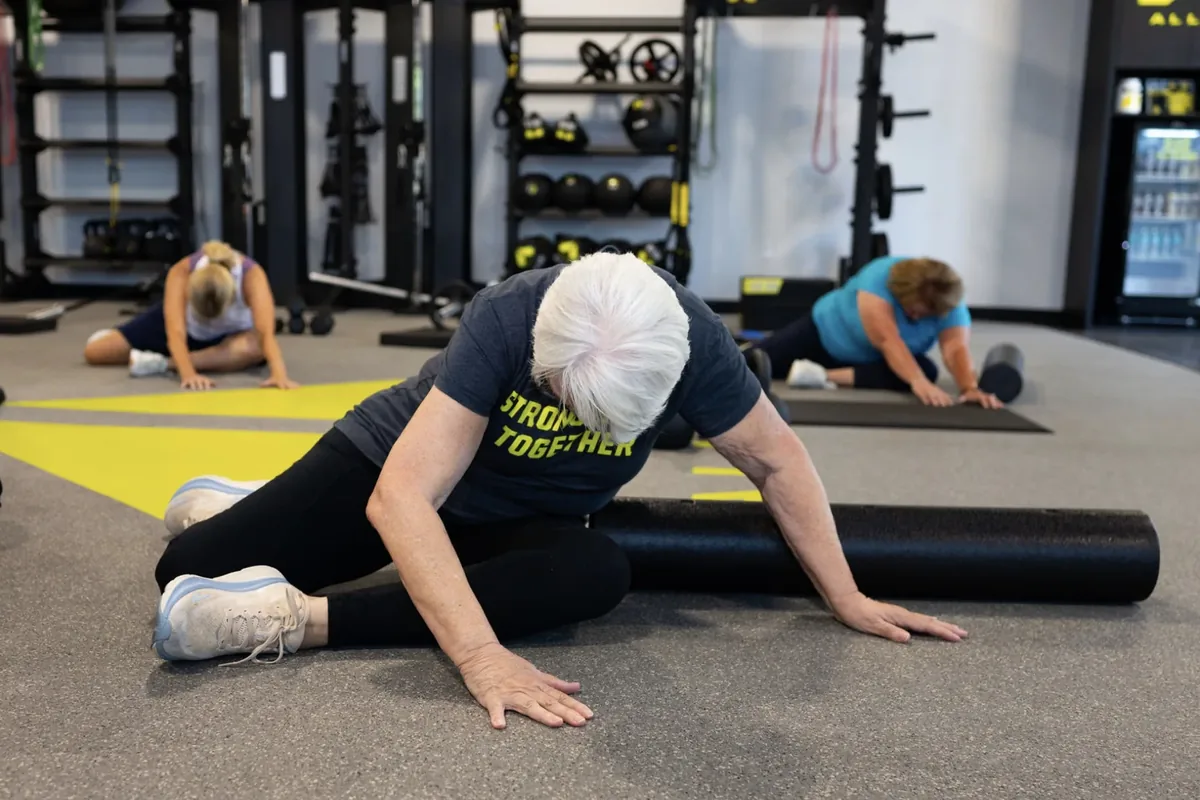 A woman in her 70s works through a seated hip mobility drill with a foam roller during a coached session
