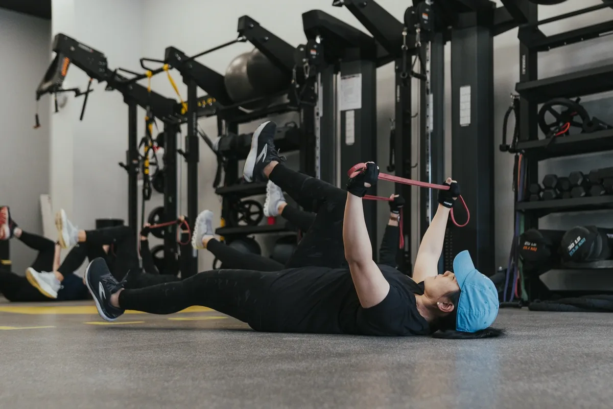 A woman lying on her back stretches one leg with a resistance band during a coached mobility session