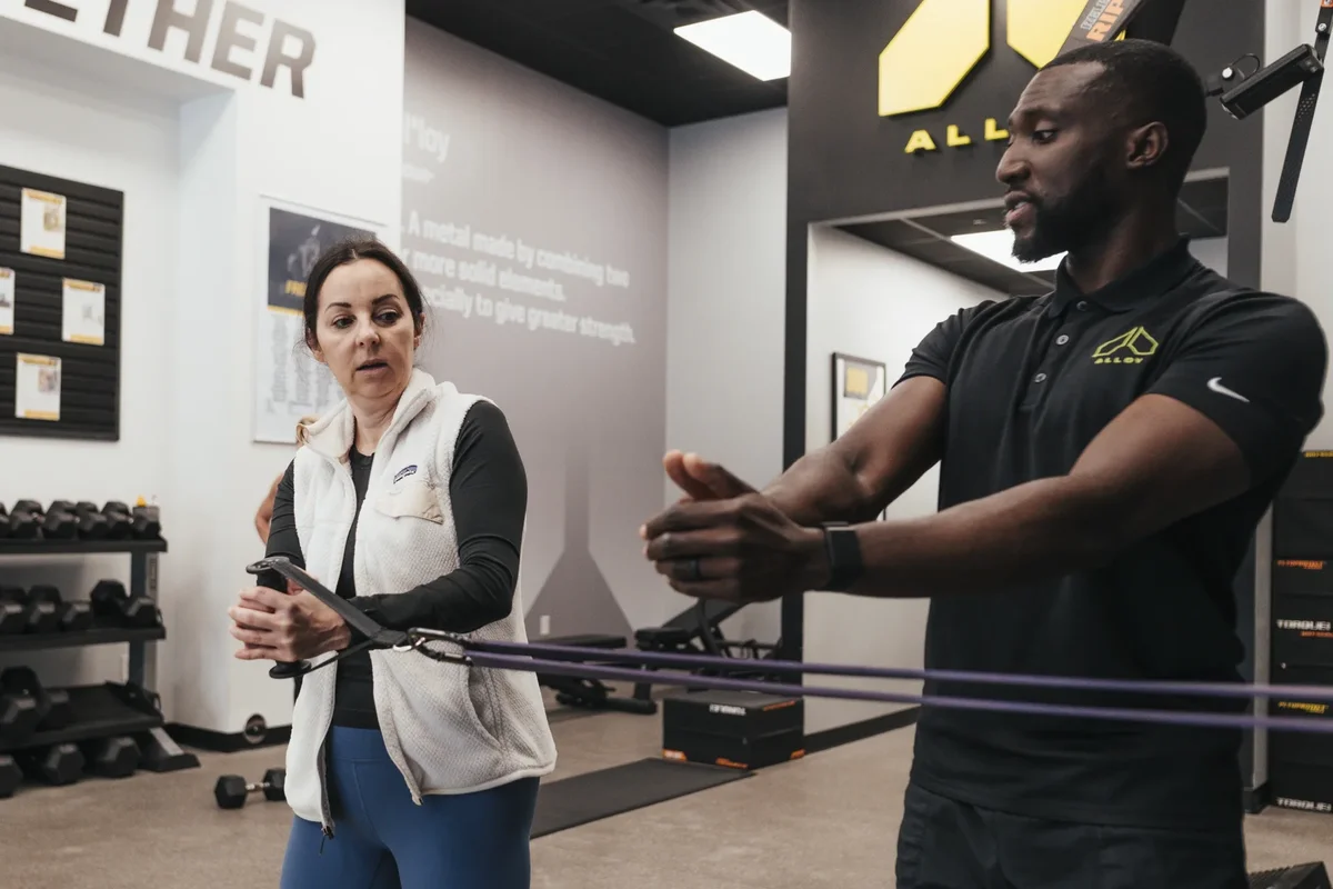 A coach guides a member through a resistance band exercise during a coached session