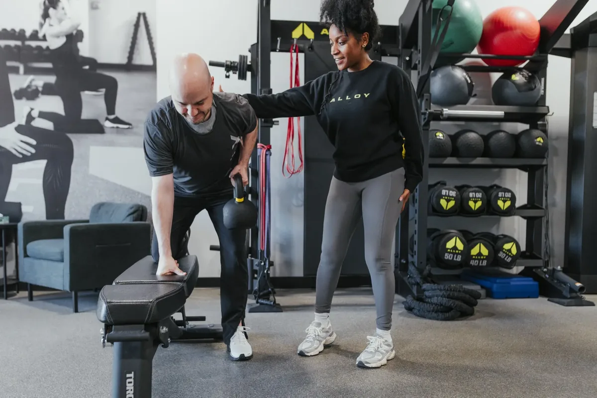 A coach guides a member through a supported single-leg hinge with a kettlebell during a training session.