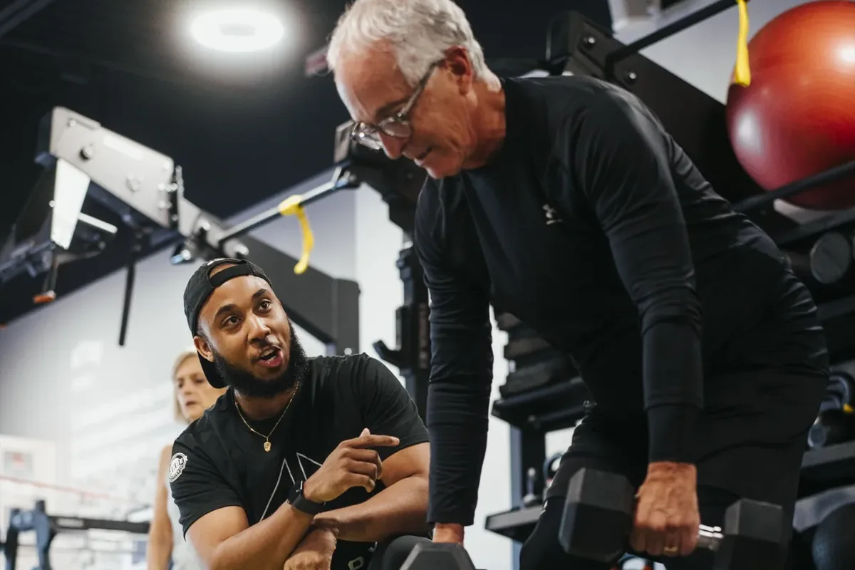 A coach talks a member through his next set of dumbbell work on the training floor.
