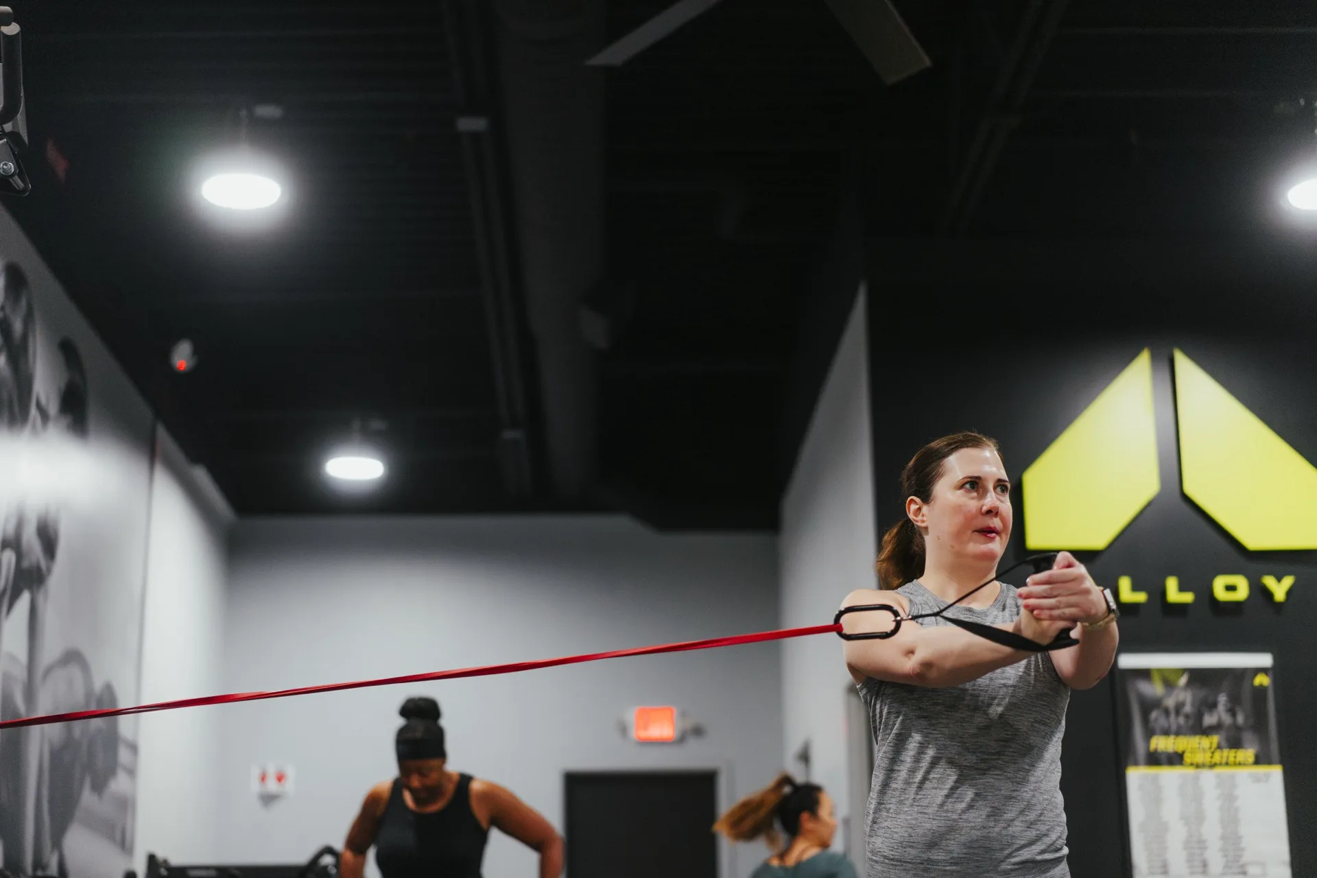 Woman pulling a red resistance band across her chest while two others train behind her