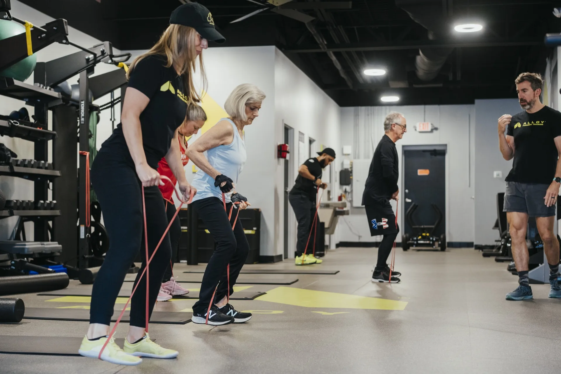 Coaches leading a small group of adults through a resistance-band squat on mats