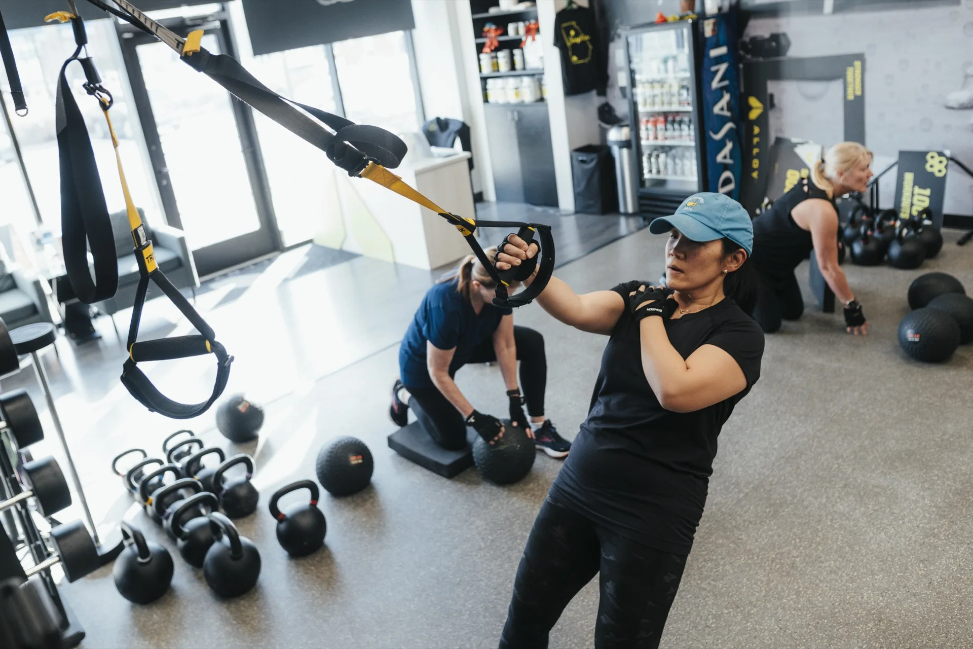 Woman pulling a TRX strap while two other women train with exercise balls behind her